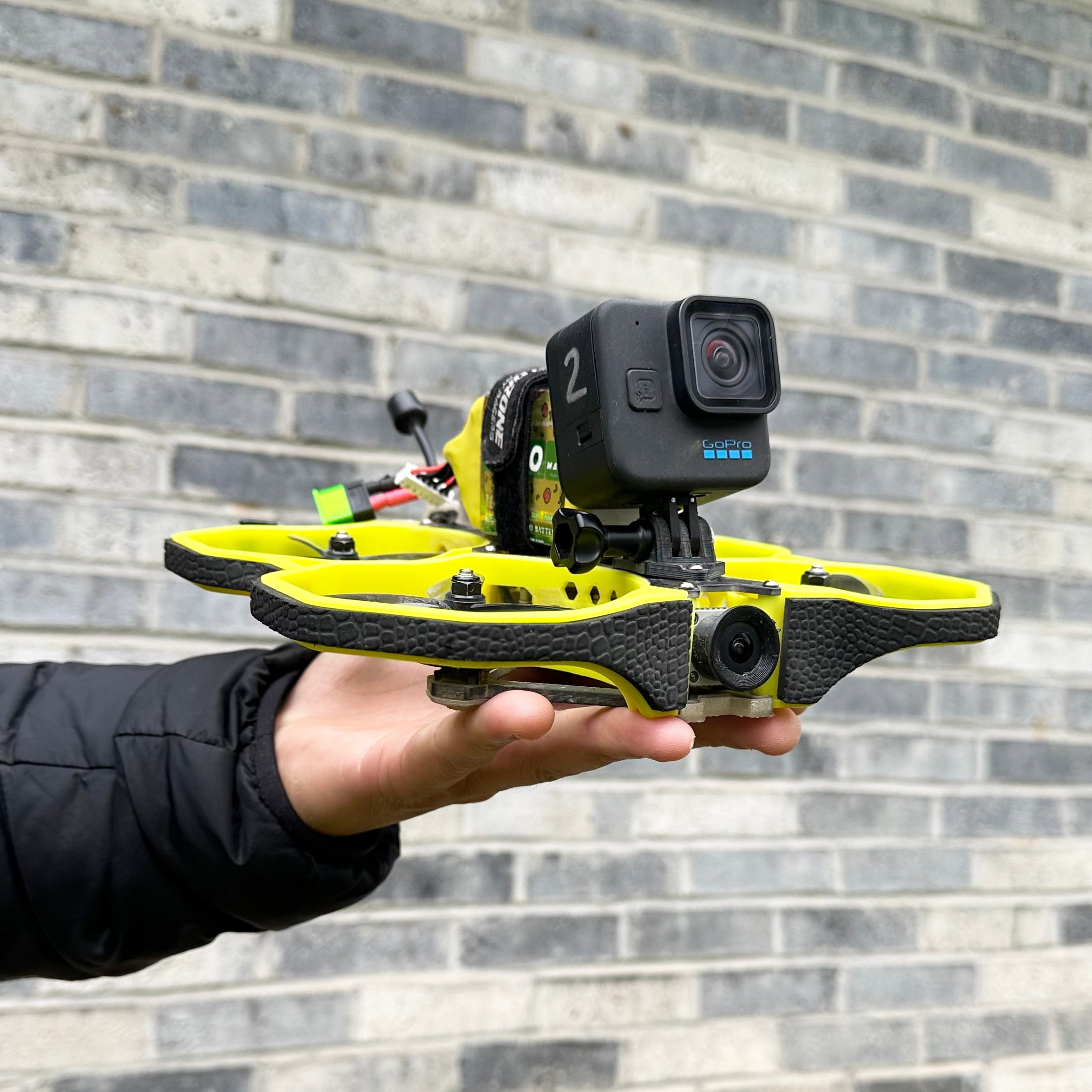 Bentonville Drone Pilot Anderson Ta hand holding drone in front of brick wall with go pro camera mounted